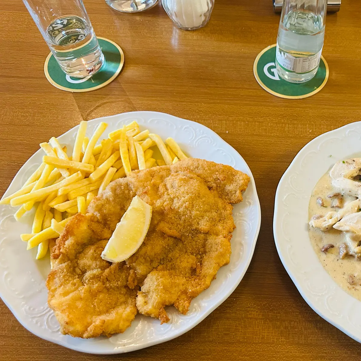 Schnitzel mit Pommes frites auf einem Holztisch, daneben Gläser auf Bierdeckeln